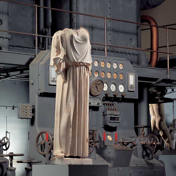 Statua vestita di peplo davanti a motore diesel